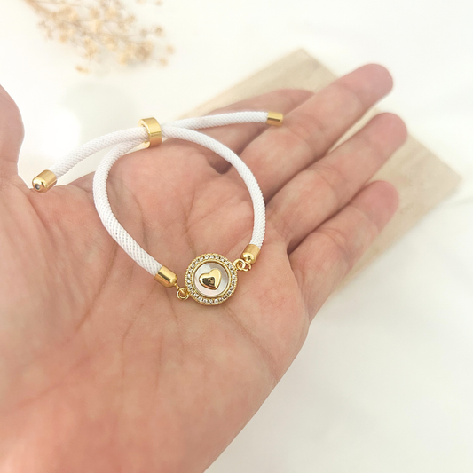 White cord bracelet with pavé heart medallion held in hand