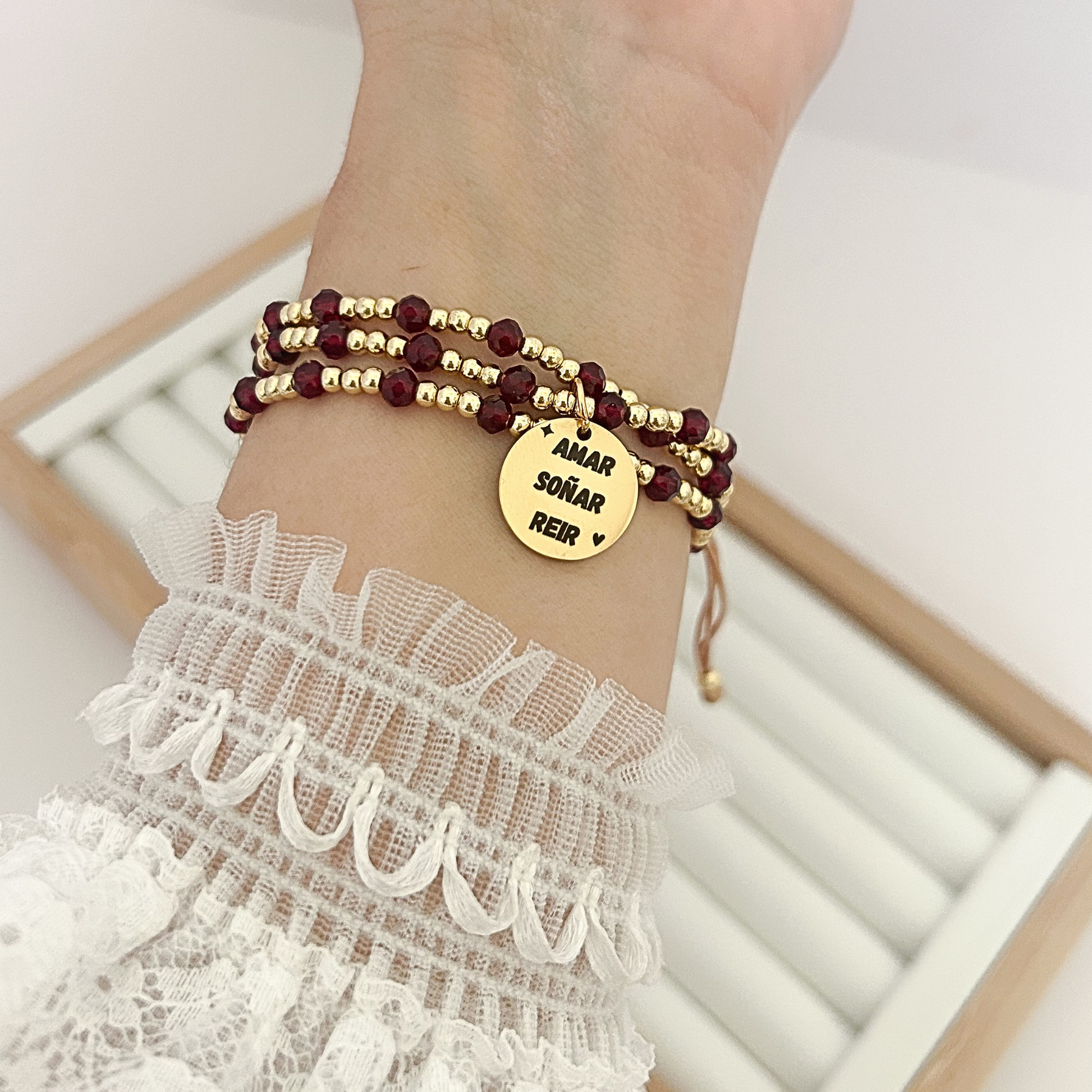 Women’s burgundy crystal bead bracelet with gold details and inspirational charm worn on wrist.