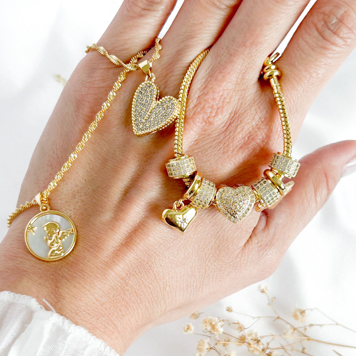 Gold charm bracelet with crystal hearts, paired with delicate gold heart and angel necklaces, meaningful everyday jewelry for women.